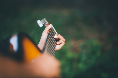 Cropped hand of person playing guitar over field