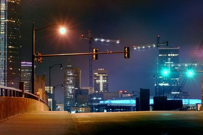 Illuminated street amidst buildings against sky at night