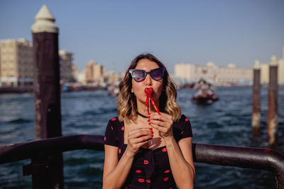 Woman holding heart shape against river in city