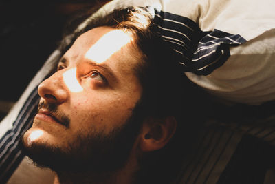 Young man looking away while lying on bed