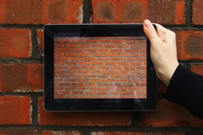 Cropped image of hand holding digital tablet with brick wall picture