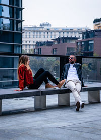 Friends sitting on seat against buildings in city