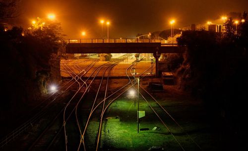 Bridge over railroad tracks amidst illuminated street lights at night