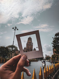 Midsection of person holding a polaroid against sky in city