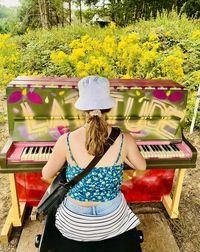 Rear view of young woman sitting playing piano 