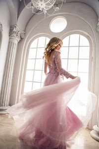 Beautiful young woman in pink lace dress spinning in the white room