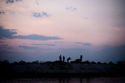 Silhouette people standing on shore against sky during sunset