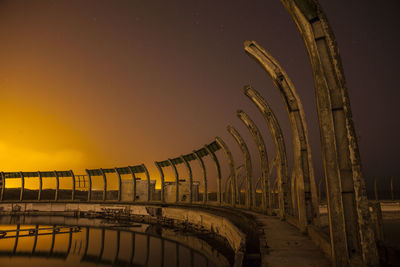 Pond by built structure against orange sky during sunset