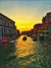 Canal in city against sky at sunset