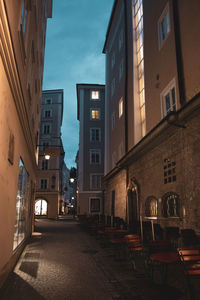 Illuminated street amidst buildings in city against sky at dusk