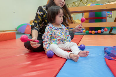 Cute girl with teacher playing on carpet in kindergarten