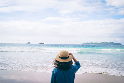 Rear view of woman standing on beach against sky