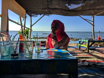 Man sitting on table by sea against sky