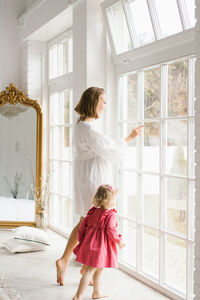 Mother and her little daughter look out the window in the living room