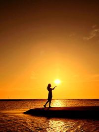 Silhouette man standing at beach against sky during sunset