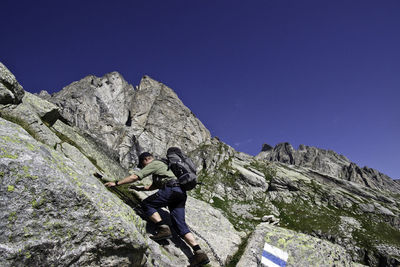 Low angle view of man climbing mountain against blue sky