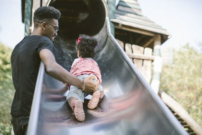 Father supporting daughter crawling up on slide at playground