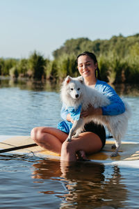 Happy cheerful woman hugging her snow-white dog japanese spitz while sitting on the sup board