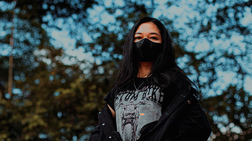 Portrait of young woman standing against trees