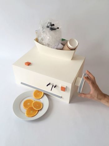 High angle view of cropped hand operating juicer with orange slices in plate on table