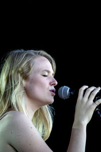 Portrait of young woman drinking against black background