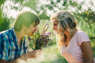 Close-up of smiling woman with flowers against trees