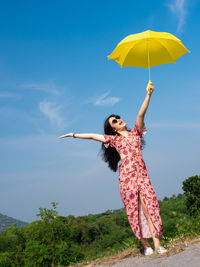 Young woman holding umbrella while standing against sky