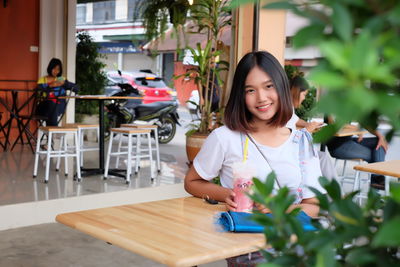 Portrait of smiling young woman sitting at sidewalk cafe