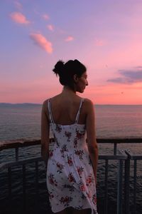 Rear view of woman standing against sea during sunset