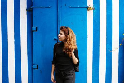 Young woman standing against blue door