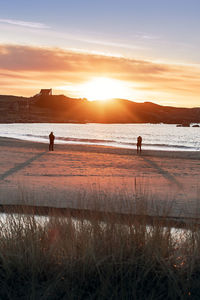 Silhouette people on beach against sky during sunset