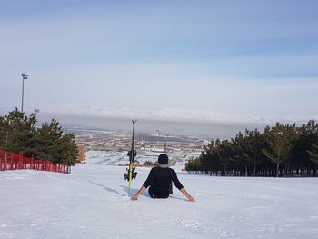 Rear view of man sitting on snowy field against sky