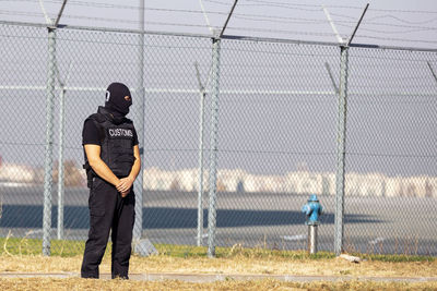 Full length of man standing by chainlink fence outdoors