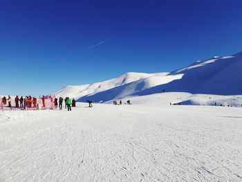 People on snowcapped mountains against blue sky