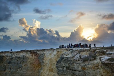 People on rocky mountain against cloudy sky during sunset