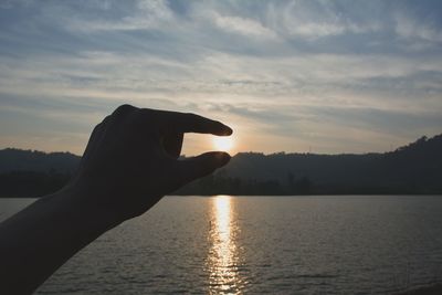 Midsection of silhouette person against lake during sunset