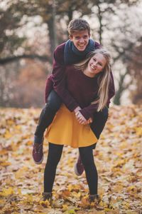 Portrait of young man piggy backing woman standing against trees during autumn