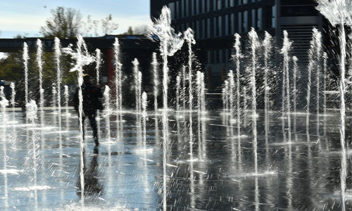 Water fountain in lake against buildings in city