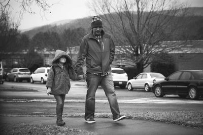 Father and son holding hands and walking on footpath in city during winter