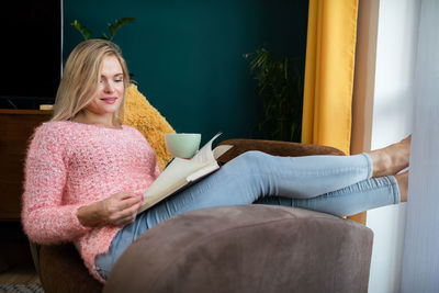 A girl reads a book with a cup in her hand while resting.
