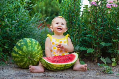 Cute girl eating watermelon sitting against plants