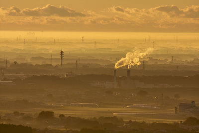 Aerial view of smoke emitting from factory against cloudy sky during sunset