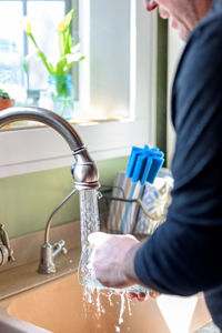 Midsection of man washing glass under faucet