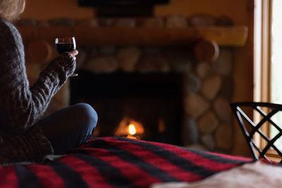 Close-up of woman sitting on bed with glass of wine in front of romantic fieldstone fireplace