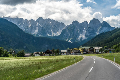 Road by houses and mountains against sky