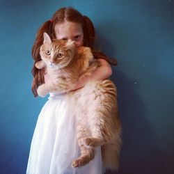 Portrait of girl holding cat and standing against wall