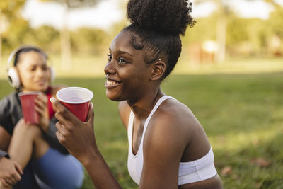 Happy young woman with disposable cup sitting in park