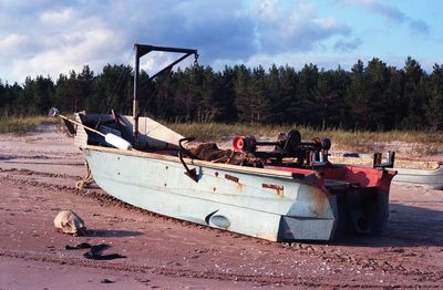 Abandoned boat moored on field against sky