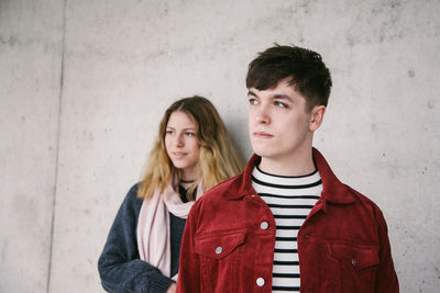 Young couple looking away while standing against wall