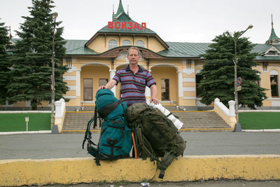 Portrait of man with backpacks standing on road in city